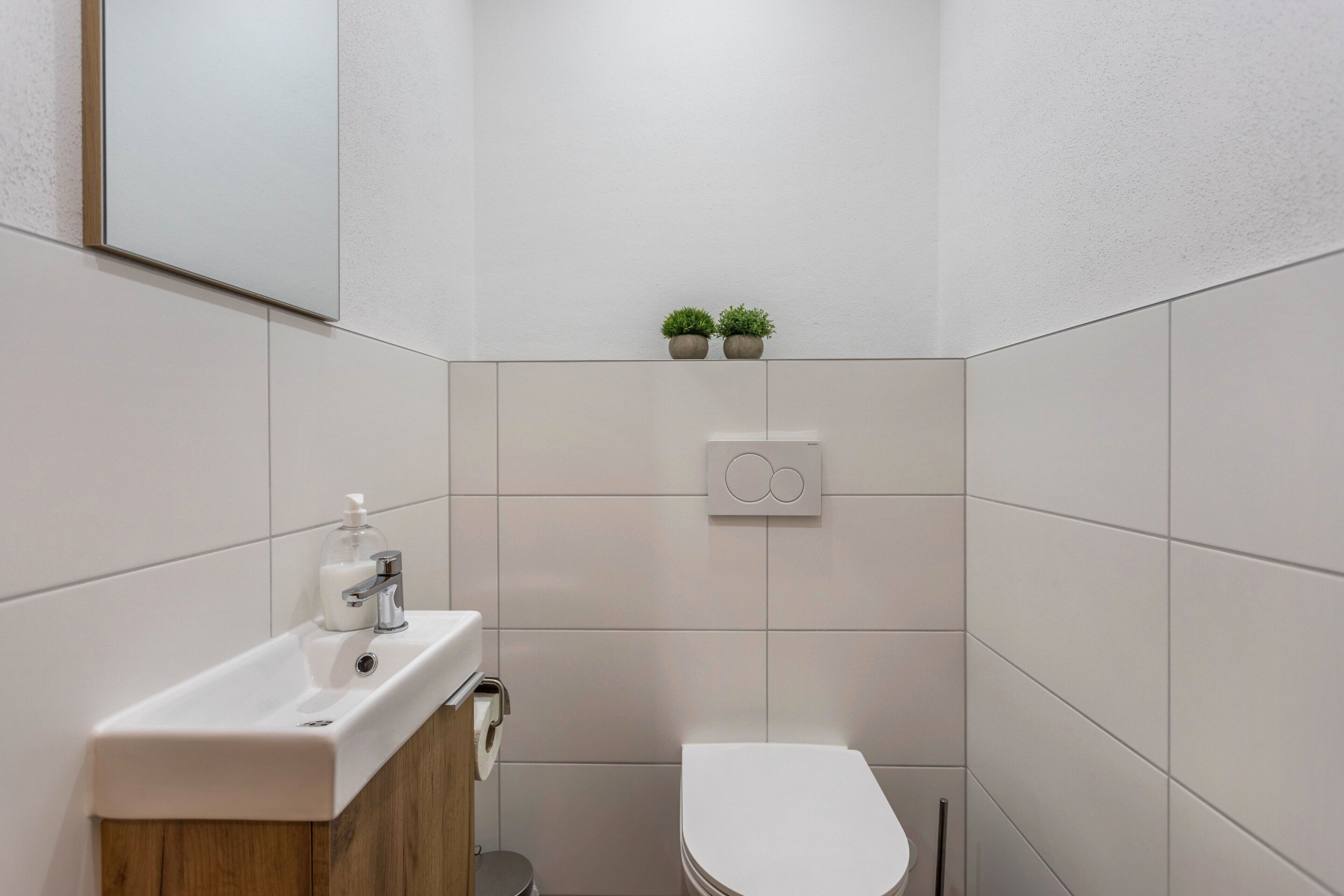 Ein Badezimmer mit Waschbecken, Toilette und zwei kleinen Topfpflanzen an der Wand.