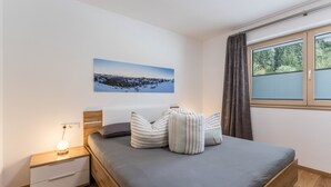 Une chambre à coucher avec un lit, une table de chevet, une lampe et une fenêtre avec des rideaux.