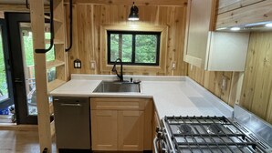 Une cuisine de taille réduite avec des murs en bois, une fenêtre, un évier, un lave-vaisselle et une cuisinière.