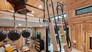 Un intérieur de chalet chaleureux avec un lit en mezzanine, une cheminée et un escalier en bois.