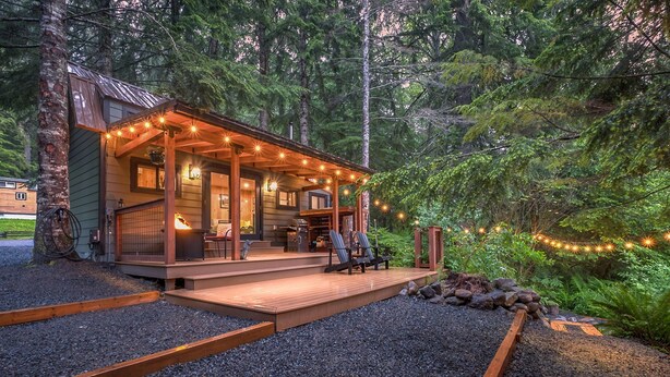 Une cabane dotée d’une terrasse en bois, de guirlandes lumineuses et offrant une vue sur la forêt.