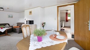 Ein Essbereich mit einem Holztisch, Stühlen, einem violetten Blumentopf und einer weißen Tischdecke.