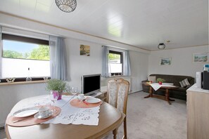 Un comedor con una mesa dispuesta para dos personas, un televisor y un sofá al fondo.