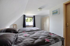 Un dormitorio con cama, ventana con cortinas, radiador, armario de madera y puerta.