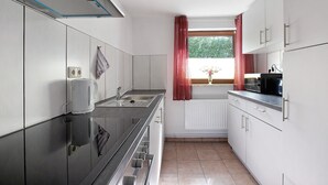 Eine moderne Küche mit weißen Schränken, einer Edelstahlspüle und einem Fenster mit roten Vorhängen.
