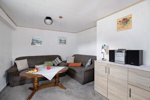 Una sala de estar con un sofá, una mesa con fruta, una mesita de centro, un mueble con estufa y dos cuadros en la pared.