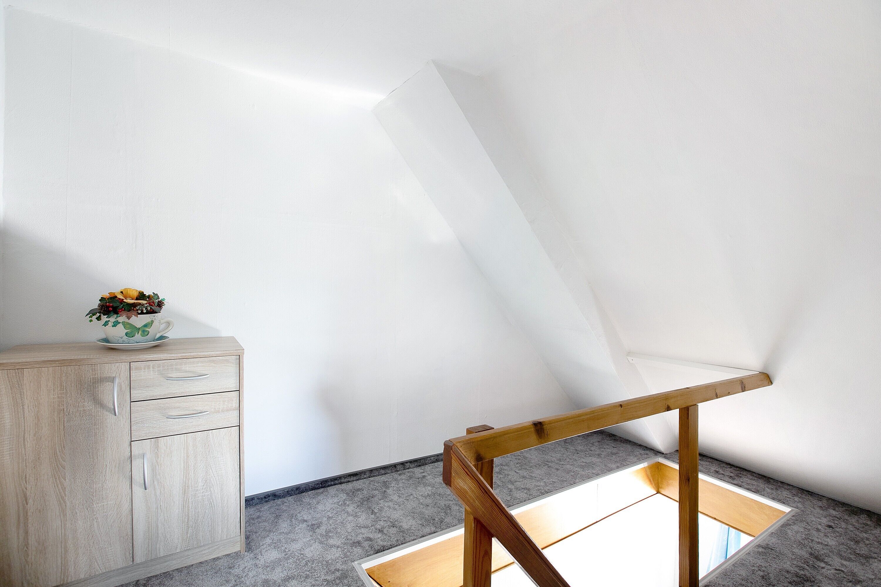 A room with a wooden cabinet, a small table with a cup and flowers, and a slanted ceiling.