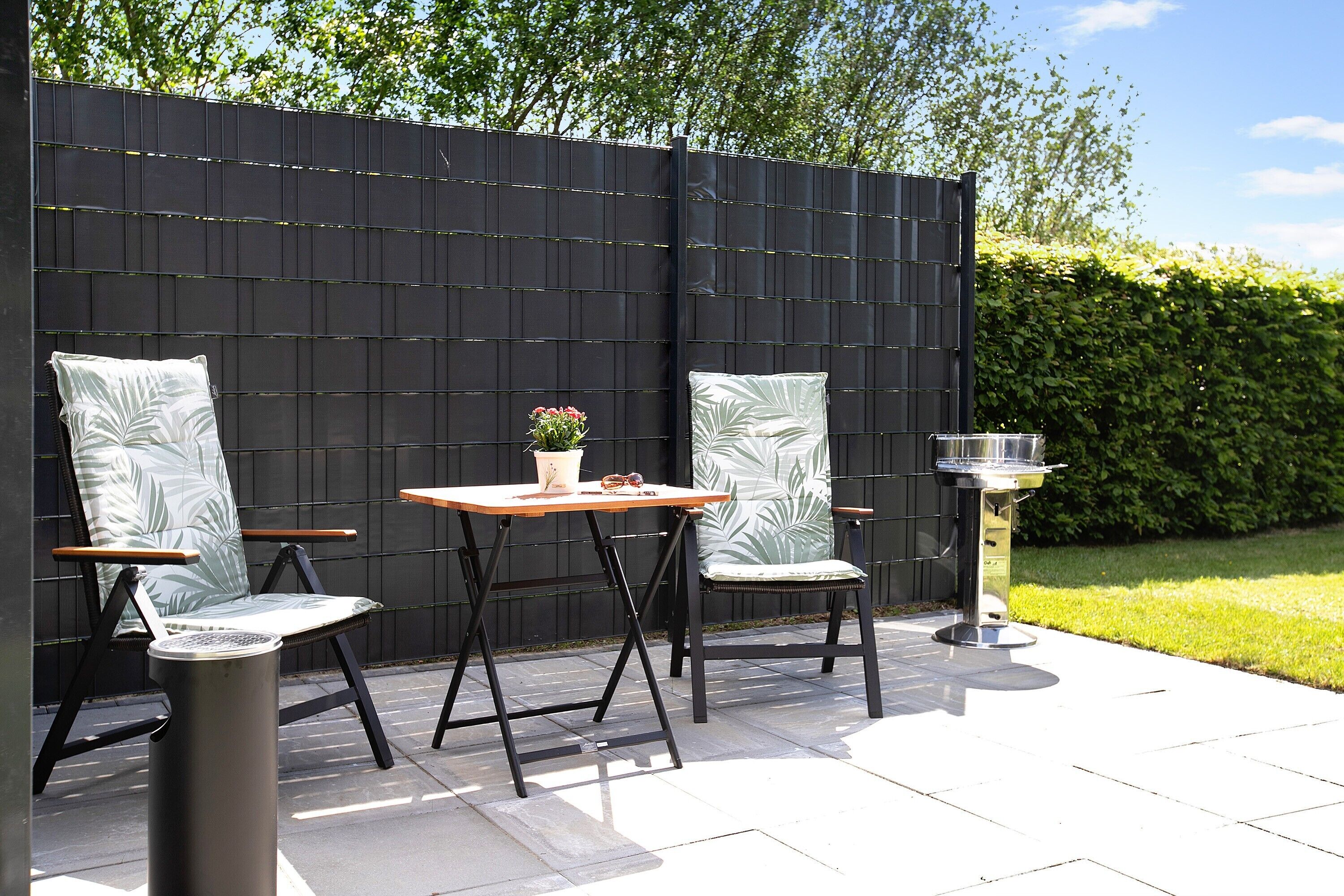 An outdoor patio with two chairs, a table, and a grill.