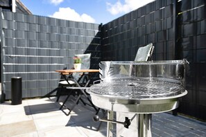 Ein Grill aus Edelstahl mit Deckel, ein Tisch, Stühle und ein Blumentopf im Garten.