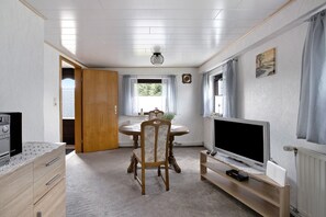 Una habitación con una mesa de comedor, sillas, un televisor, un armario de madera y un radiador.