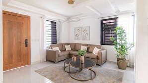 A modern living room with a sectional sofa, two round coffee tables, a wooden door, and a potted plant. - Lujo en el Centro de Bonao Piscina Privada King Bed (Bonao)