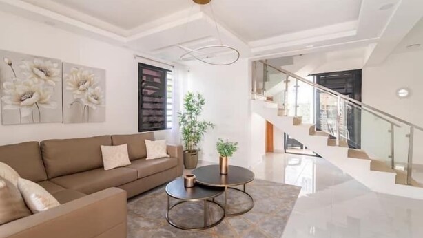 A modern living room with a sofa, two coffee tables, and a staircase. - Lujo en el Centro de Bonao Piscina Privada King Bed (Bonao)