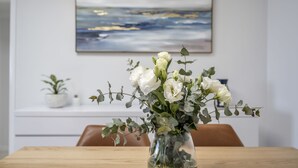 A dining table with a vase of white flowers and green leaves.