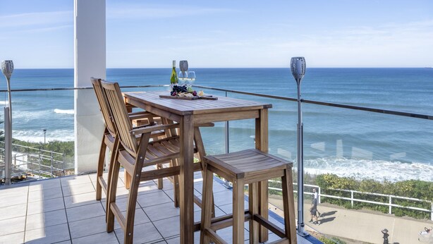 A wooden table and chairs on a balcony with a view of the ocean.