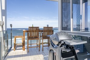 Un balcon avec une table et des chaises en bois, donnant sur l’océan.