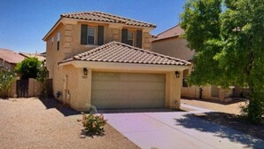 A two-story house with a tiled roof, a garage, and a small garden with flowers.