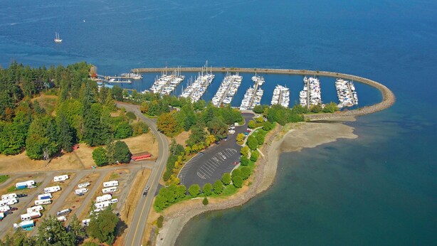 Luchtbeeld van een jachthaven met veel boten afgemeerd, omringd door groen en een parkeerplaats met campers.