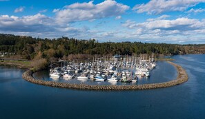 A marina with numerous boats docked, surrounded by a rocky breakwater and dense forest. - Epic Vacay! King Unit, Breakfast, Spa & Wellness Center, Close to Attractions (Sequim)