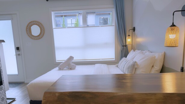 Ein Hotelzimmer mit Bett, Holztisch, Stuhl, Lampe und einem fensterbepflanzten Fenster.