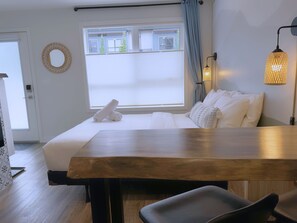 A hotel room with a bed, a wooden table, a chair, a lamp, and a window with curtains.