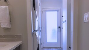 Ein schmaler Flur mit Waschmaschine, einer Tür mit Milchglas und einem weißen Handtuch an der Wand.