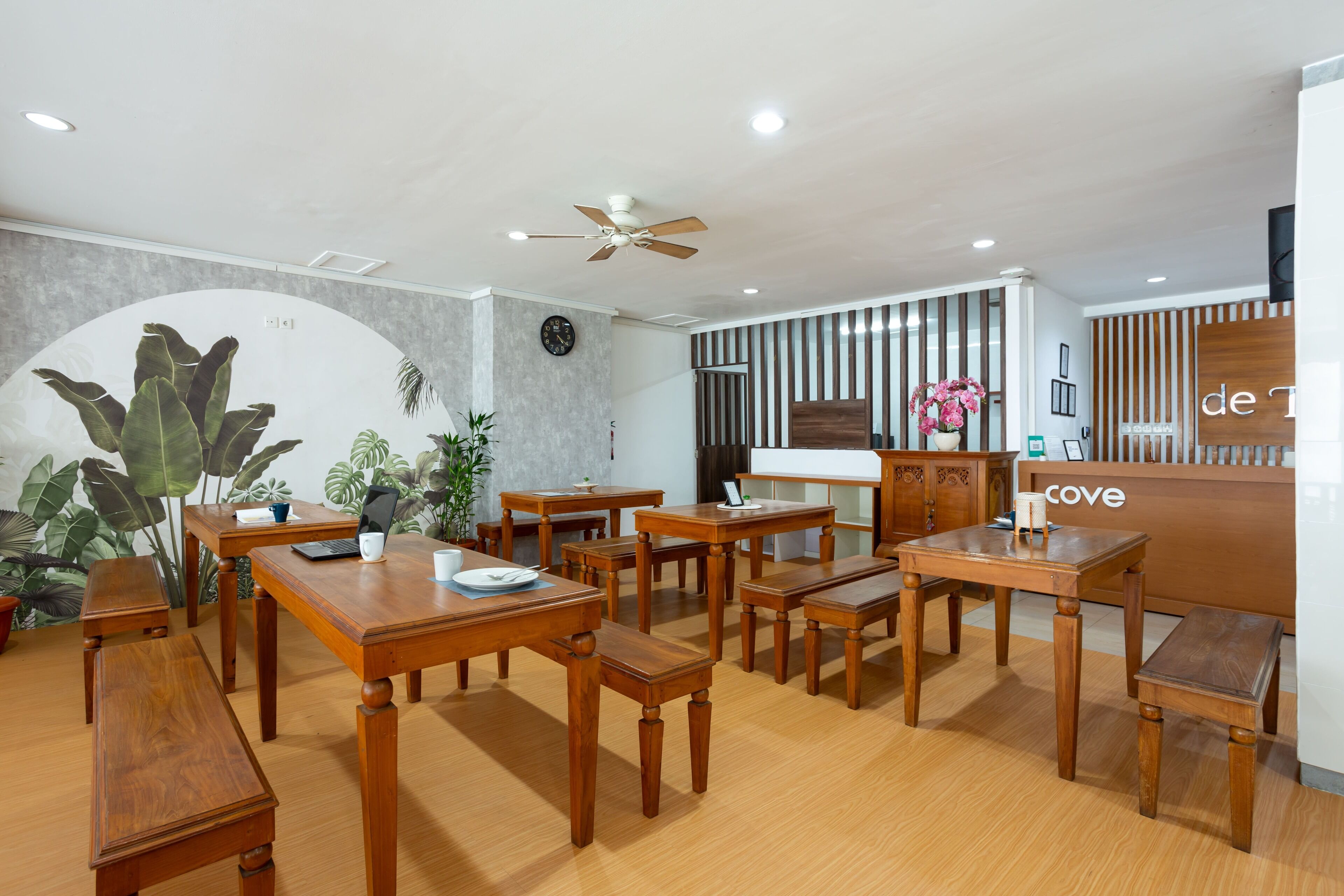 A reception area with wooden furniture, a clock, and a reception desk labeled 'de T' and 'cove'.