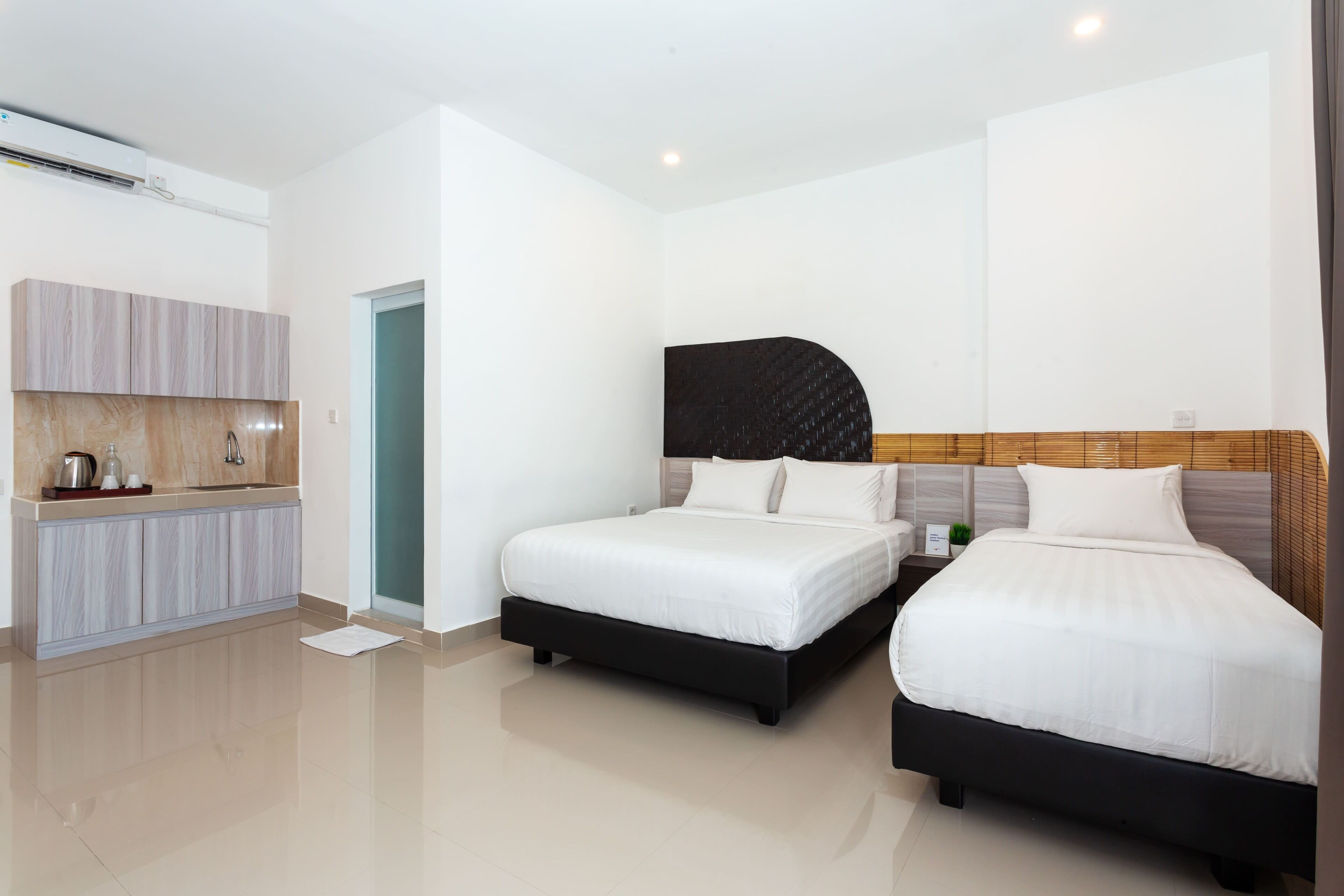 A modern hotel room with two single beds, a built-in wardrobe, a kitchenette, and a large window.