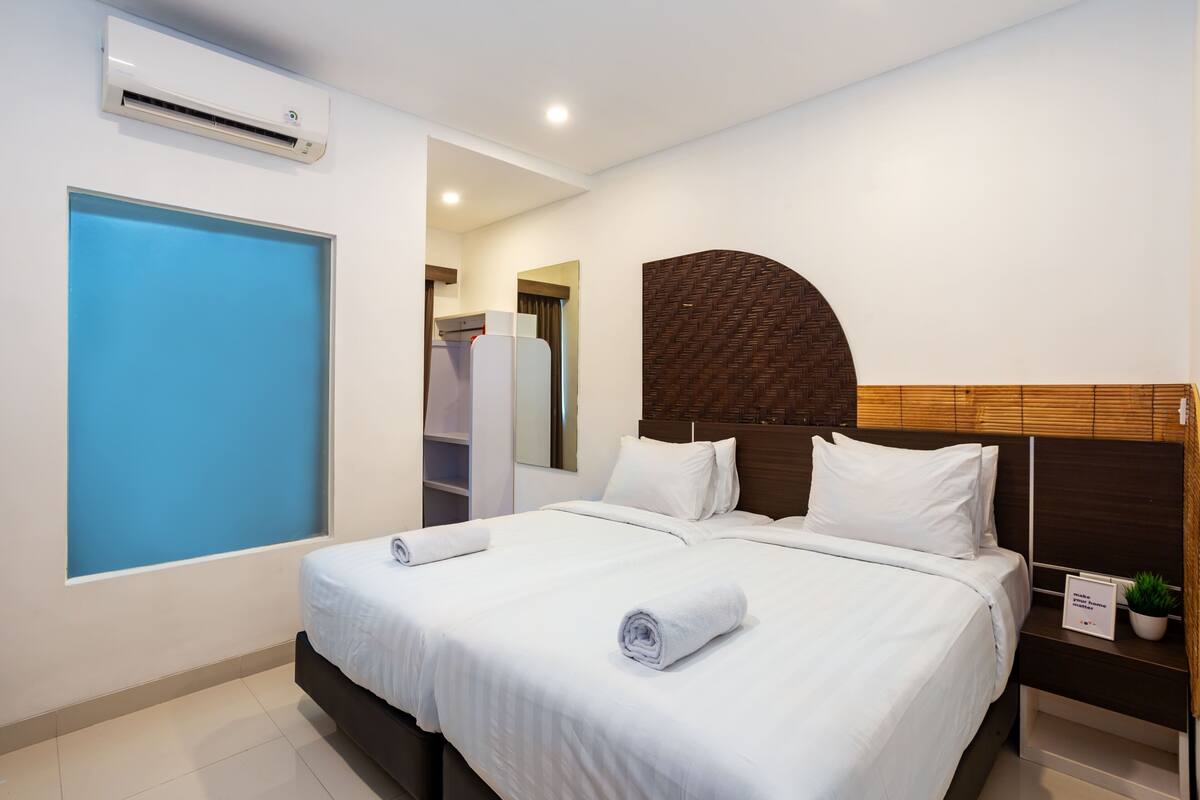 A modern hotel room with a large bed, a built-in wardrobe, and a small potted plant on the nightstand.