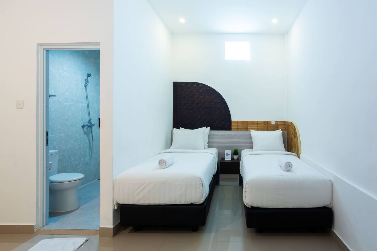 A hotel room with two beds, a shower, and a toilet.