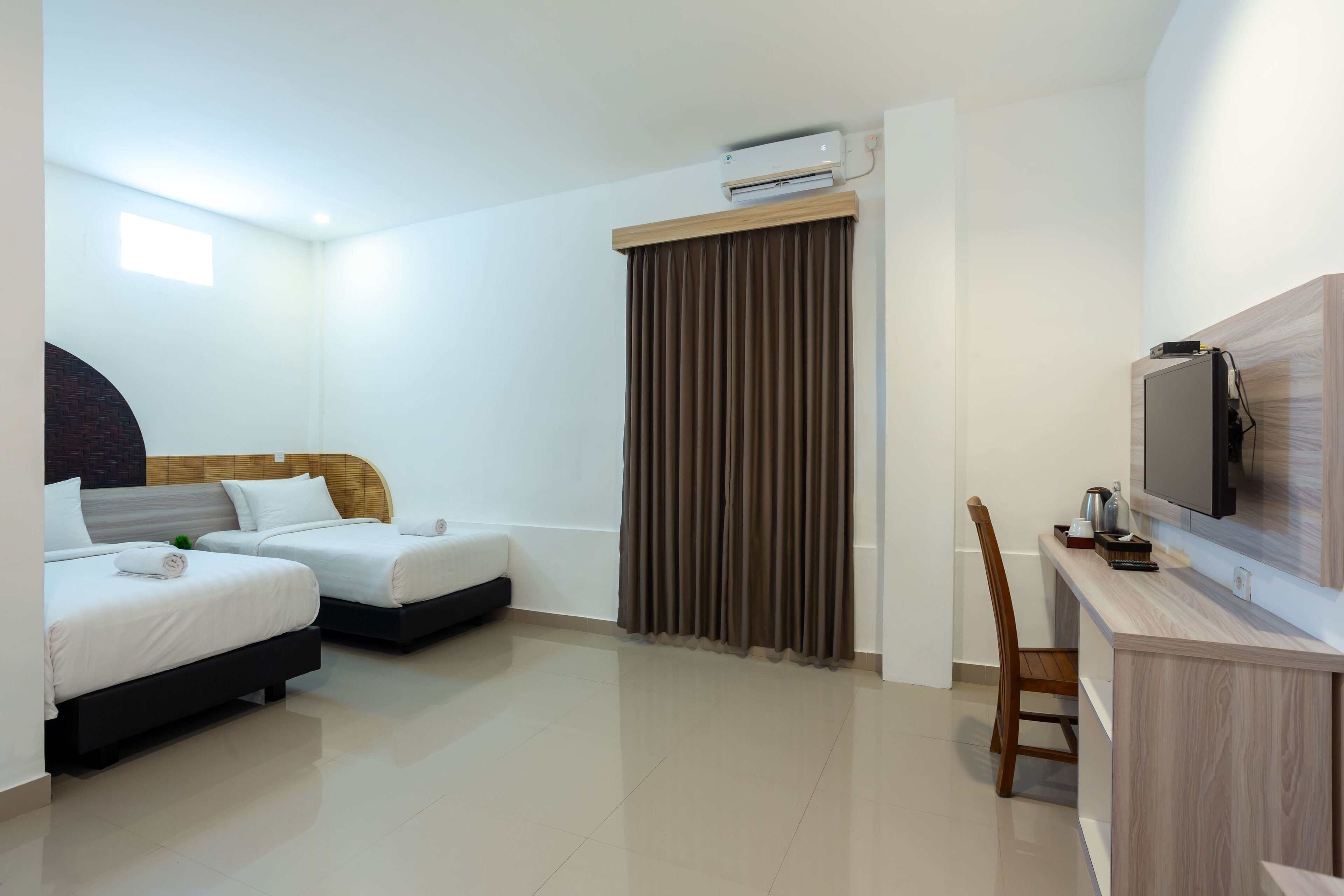 A hotel room with two beds, a desk with a television, and an air conditioning unit.
