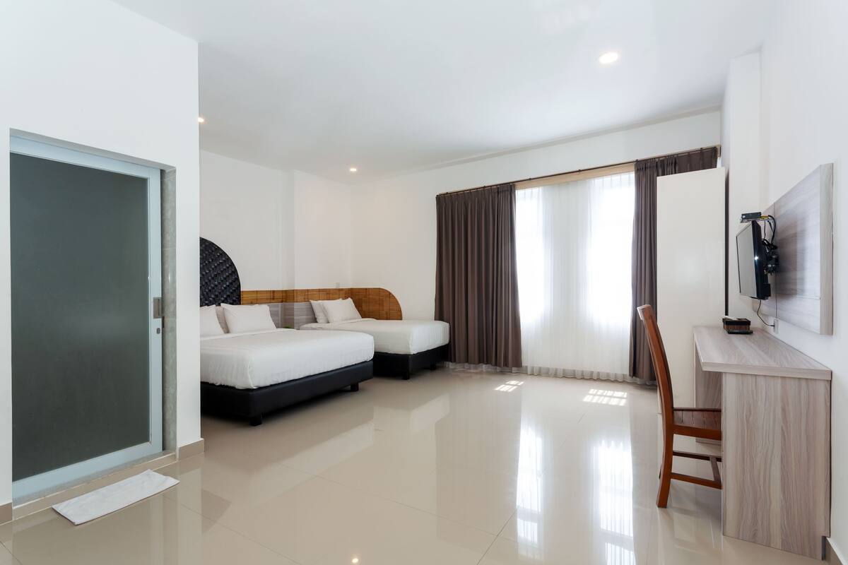 A hotel room with two beds, a desk, a chair, a TV, and a sliding door.