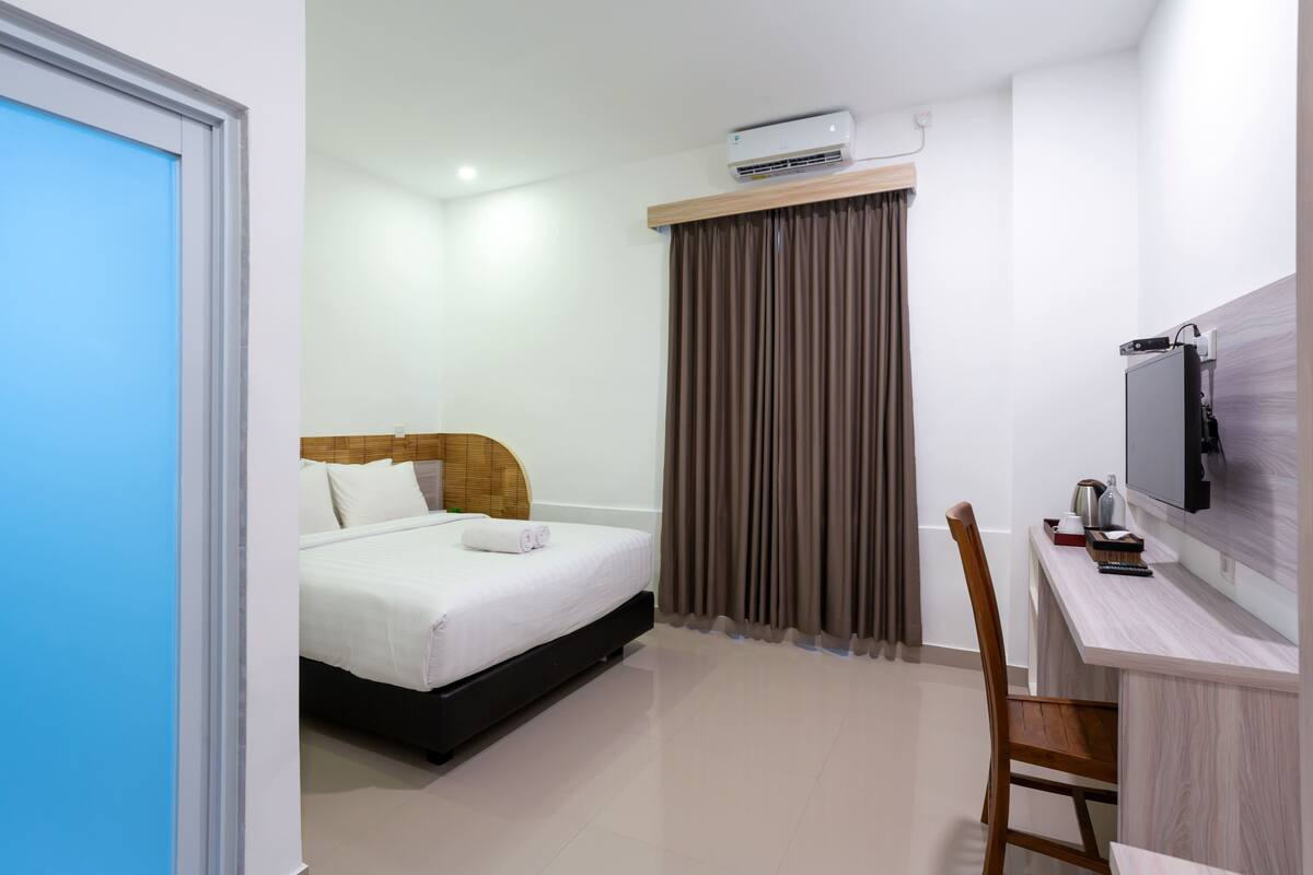 A hotel room with a bed, a desk, a chair, and a television.