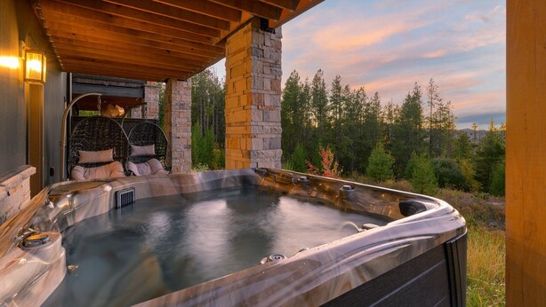 Ein Whirlpool unter einer hölzernen Pergola mit einer Stein Säule, umgeben von einer bewaldeten Landschaft.