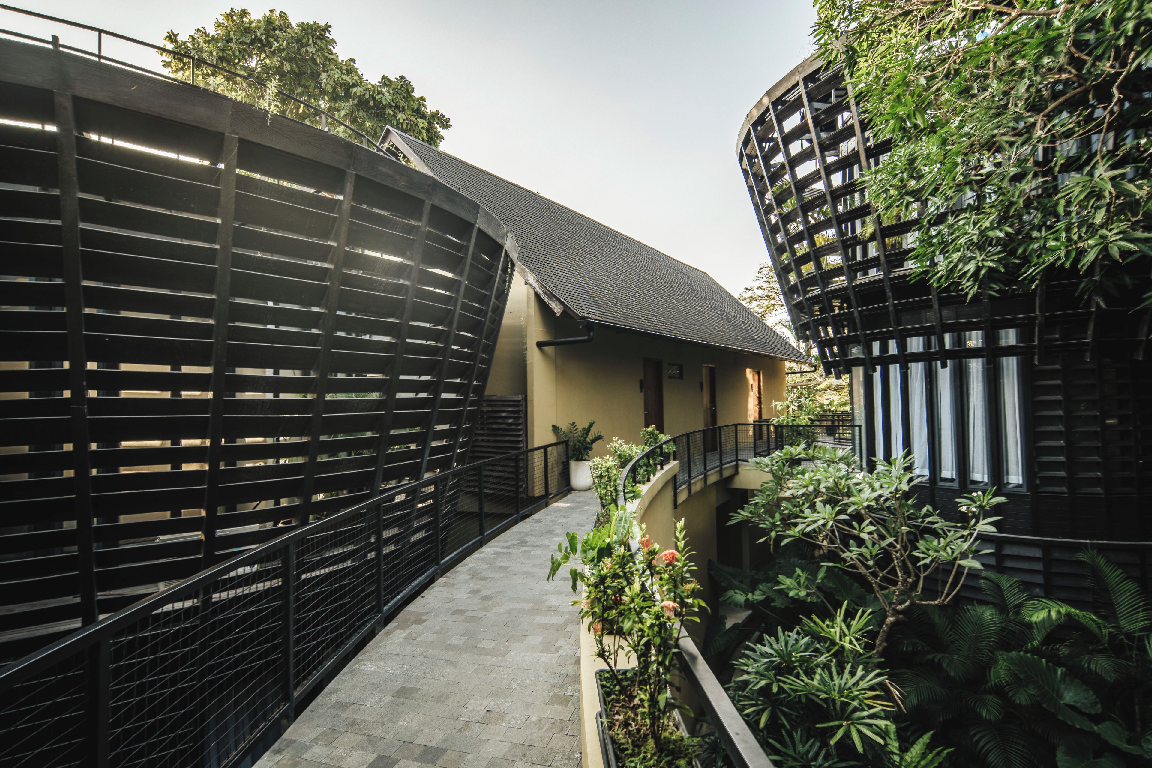 A curved pathway flanked by black metal railings, leading to a building with a sloped roof and a small balcony.