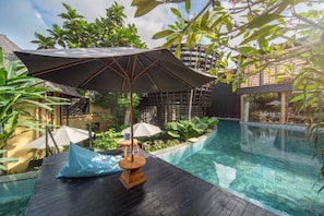 Un área de piscina al aire libre con una terraza de madera, sillones de descanso y sombrillas.