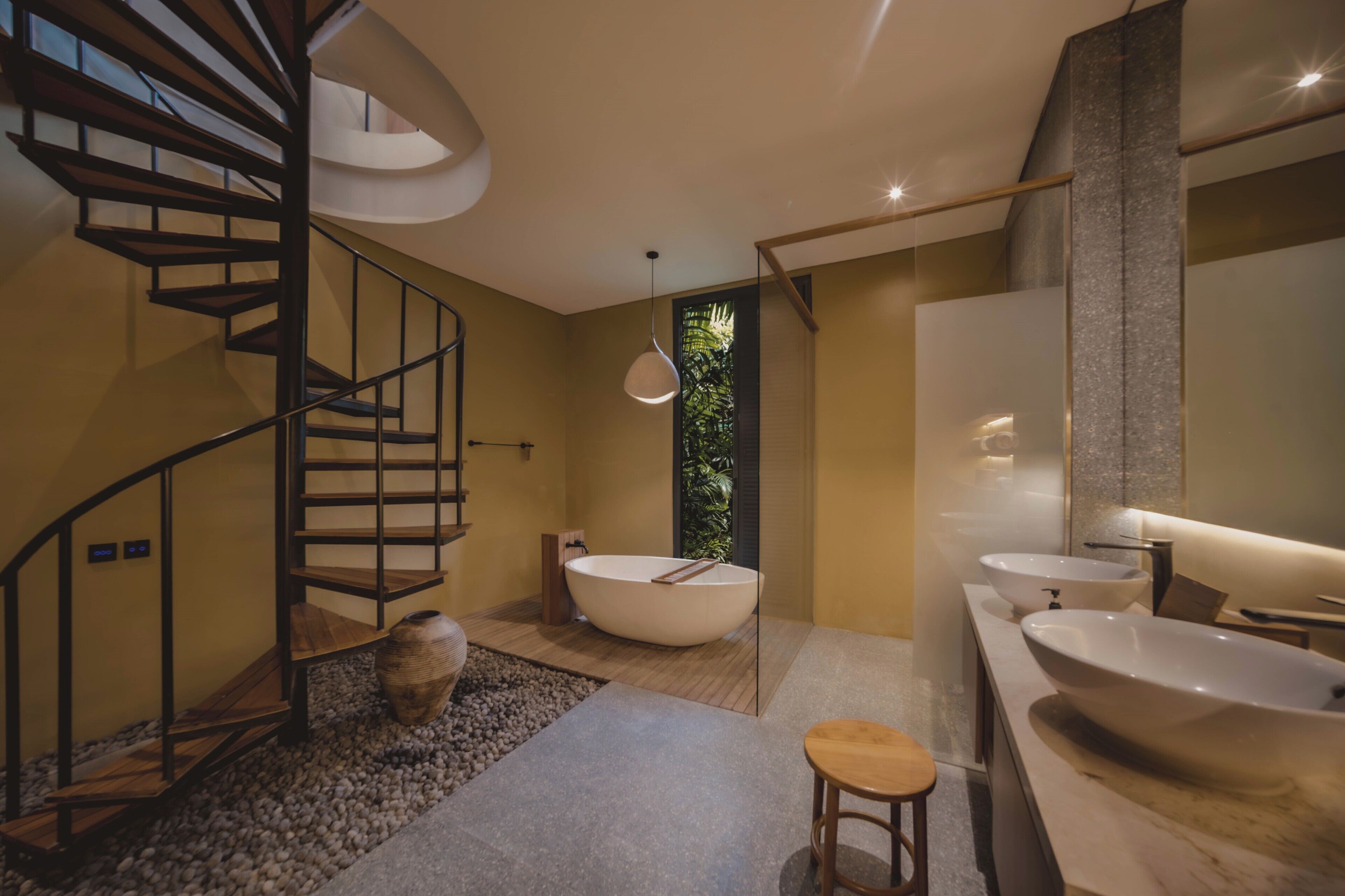 A modern bathroom with a spiral staircase, a freestanding bathtub, and two large sinks.