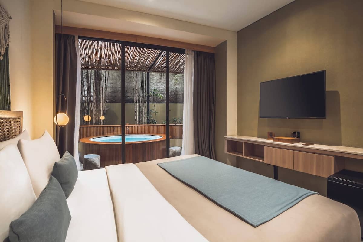Ein modernes Hotelzimmer mit einem großen Bett, einem Flachbildfernseher, einem kleinen Schreibtisch und Blick auf eine Whirlpool-Anlage und einen Außenbereich.