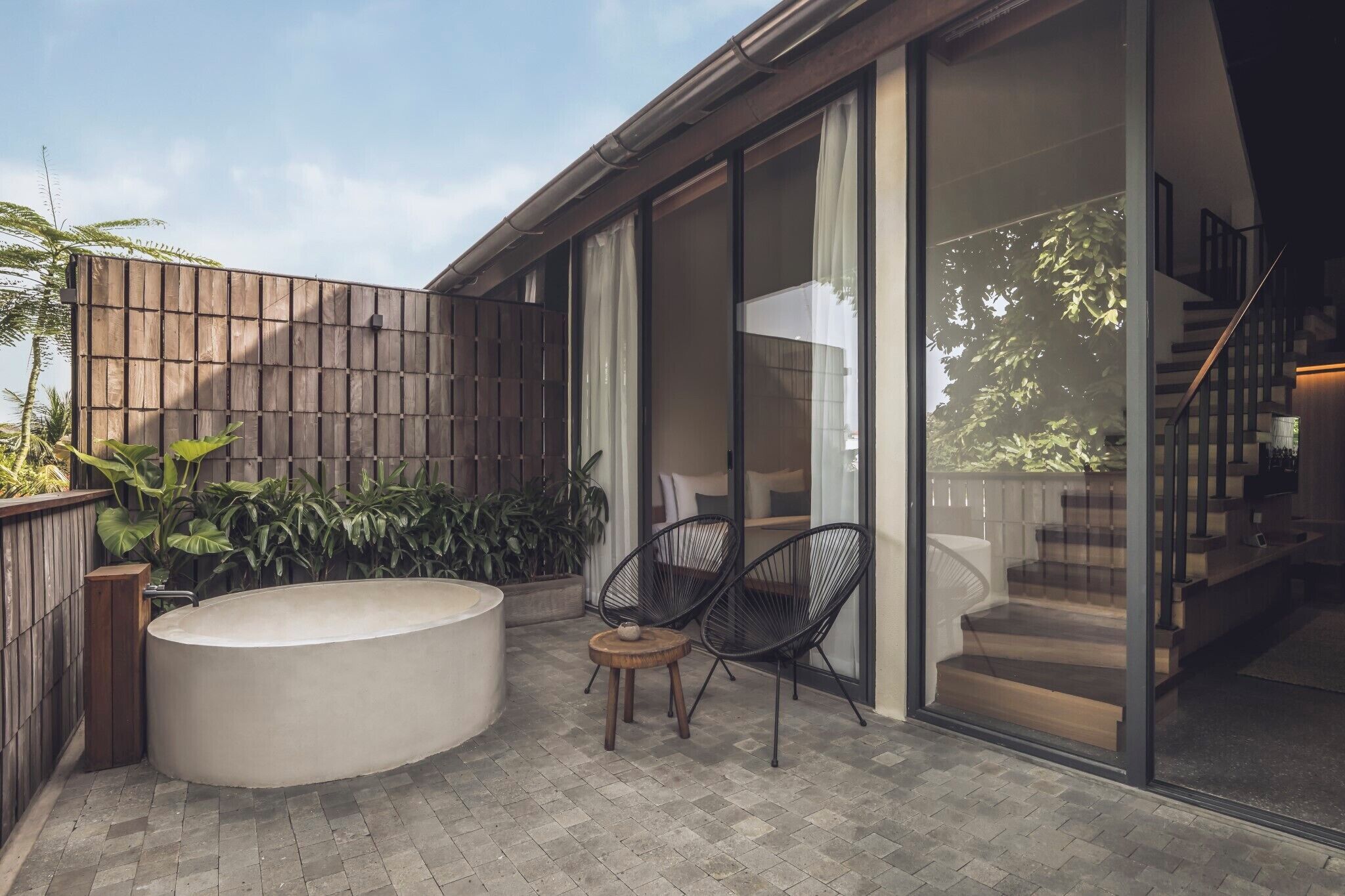 A modern outdoor patio with a hot tub, two chairs, and a wooden fence.
