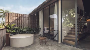 A modern outdoor patio with a hot tub, two chairs, and a wooden fence.