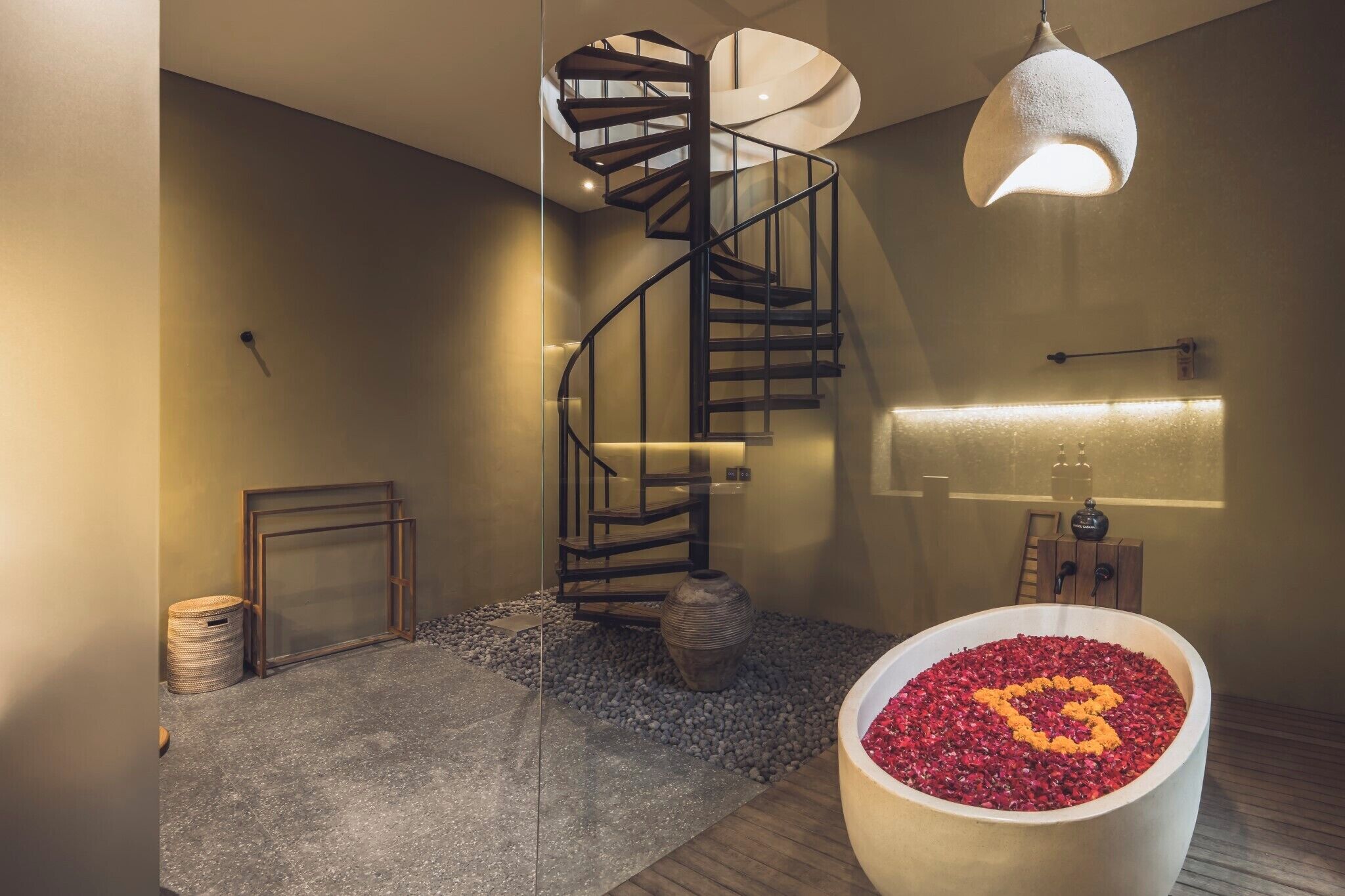 A modern interior with a spiral staircase, a large potted plant, and a decorative water feature.