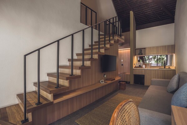 A modern interior with a wooden staircase, a flat-screen TV, a kitchen area, and a seating area.