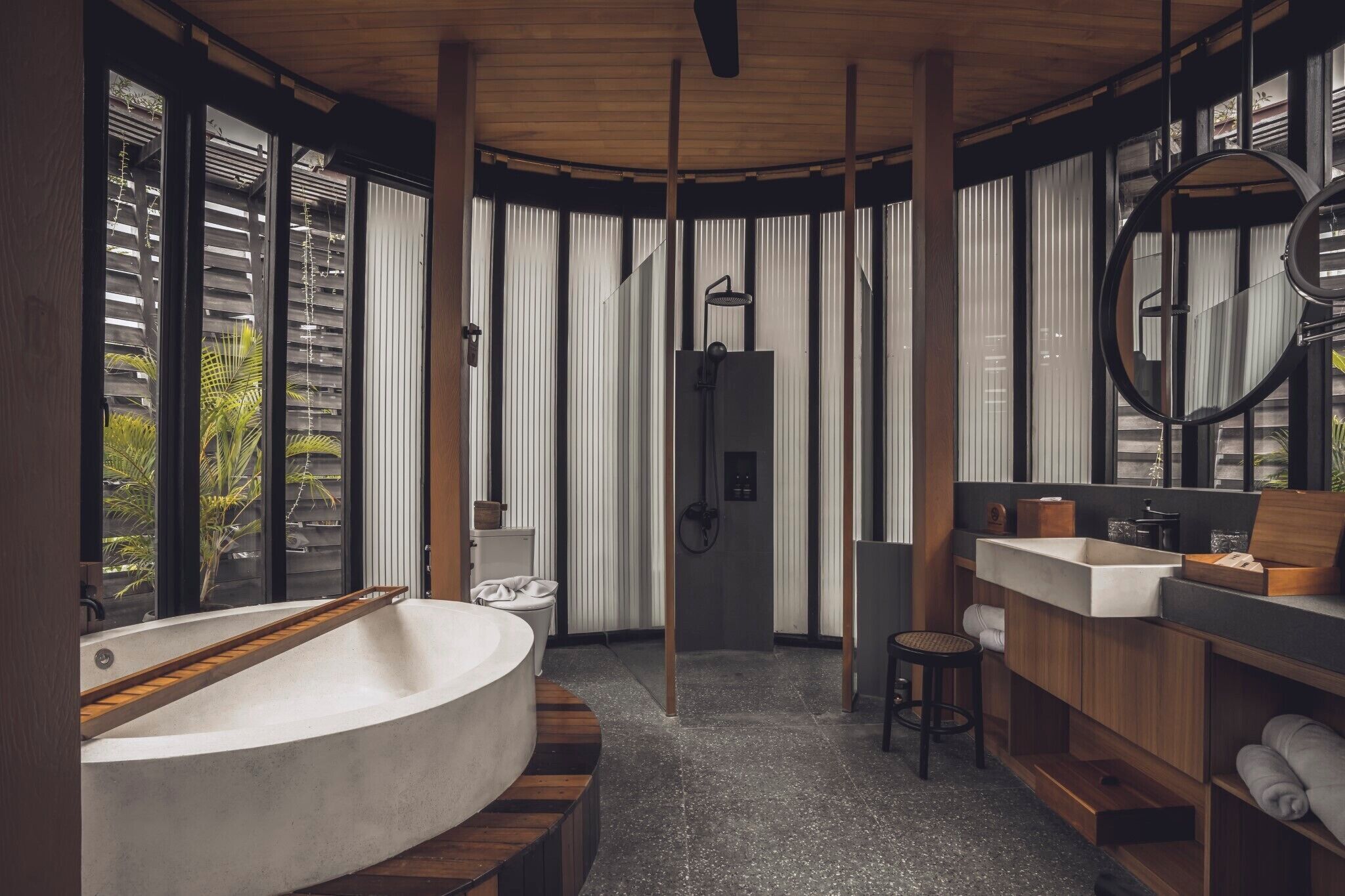 A modern bathroom with a freestanding bathtub, wooden accents, a large mirror, and a view of greenery outside.