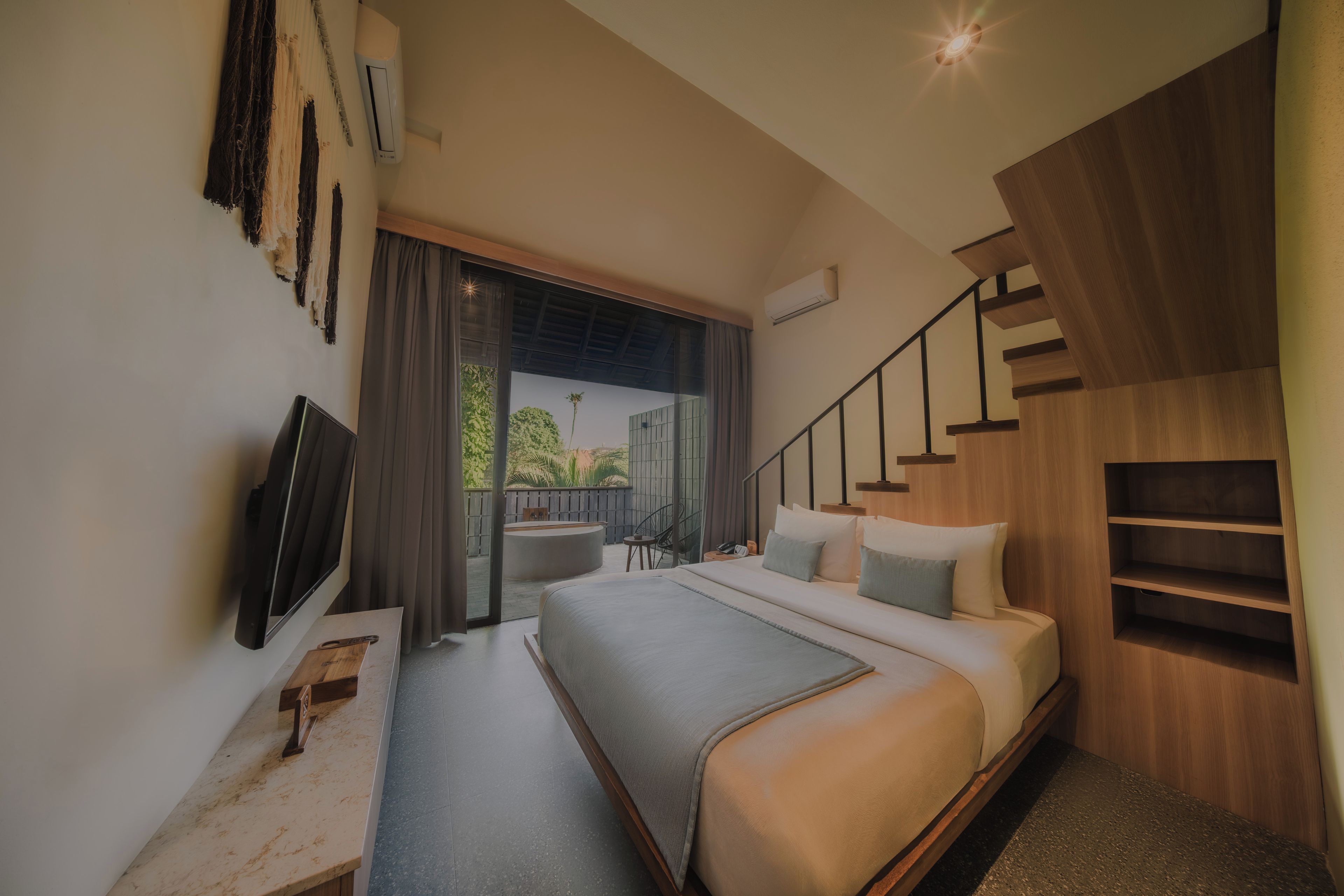 A modern bedroom with a large bed, a TV, and a view of the outdoors.
