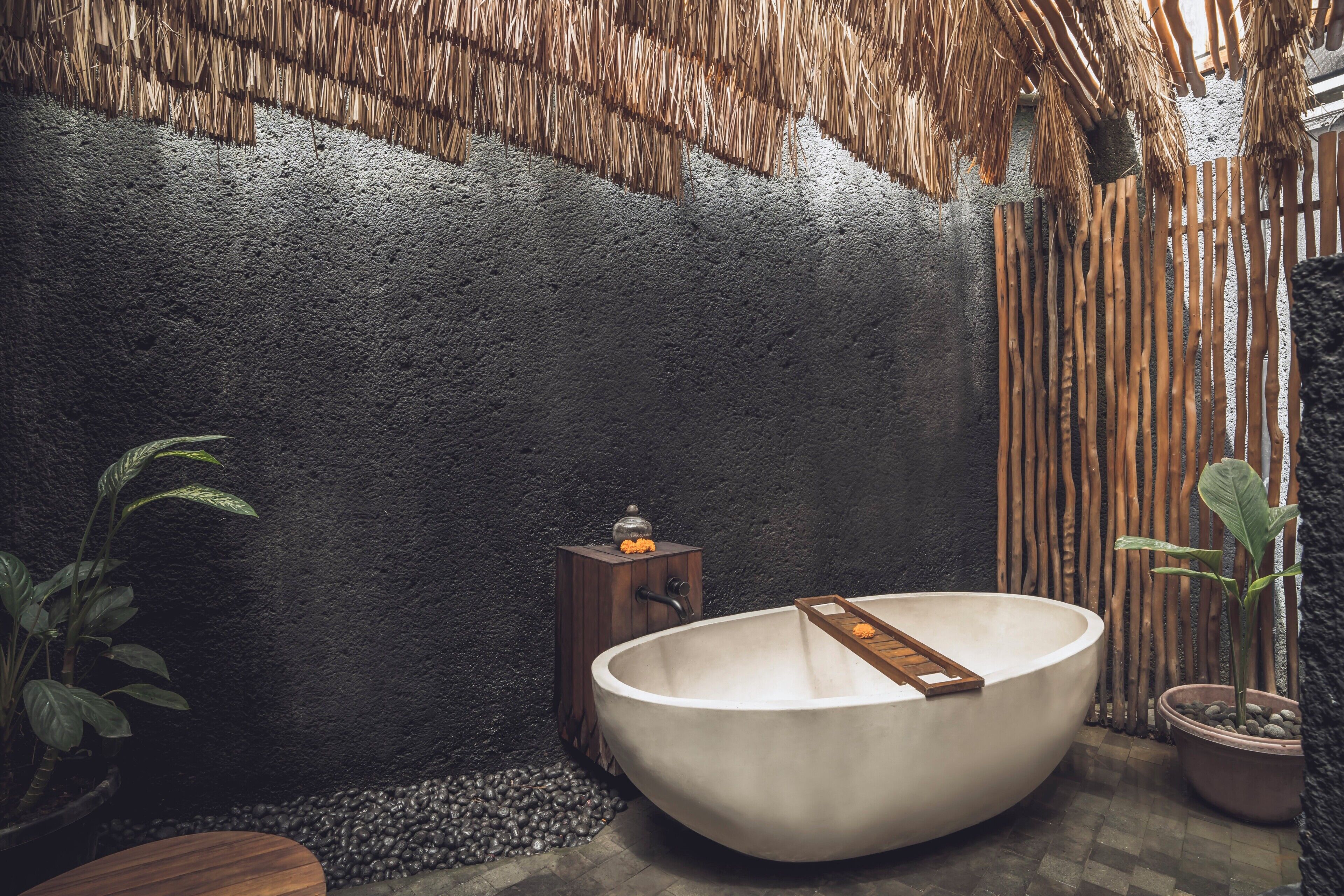 Eine Badewanne in einem Zimmer mit strukturierter Wand, einem kleinen Holzschemel und einem Blumentopf.