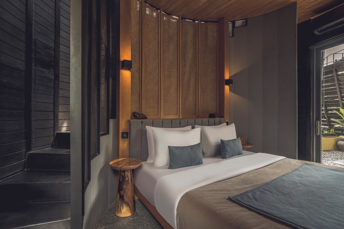 Ein modernes Schlafzimmer mit einem großen Bett, einem Holz-Kopfteil und Blick auf einen Garten durch eine Glastür.