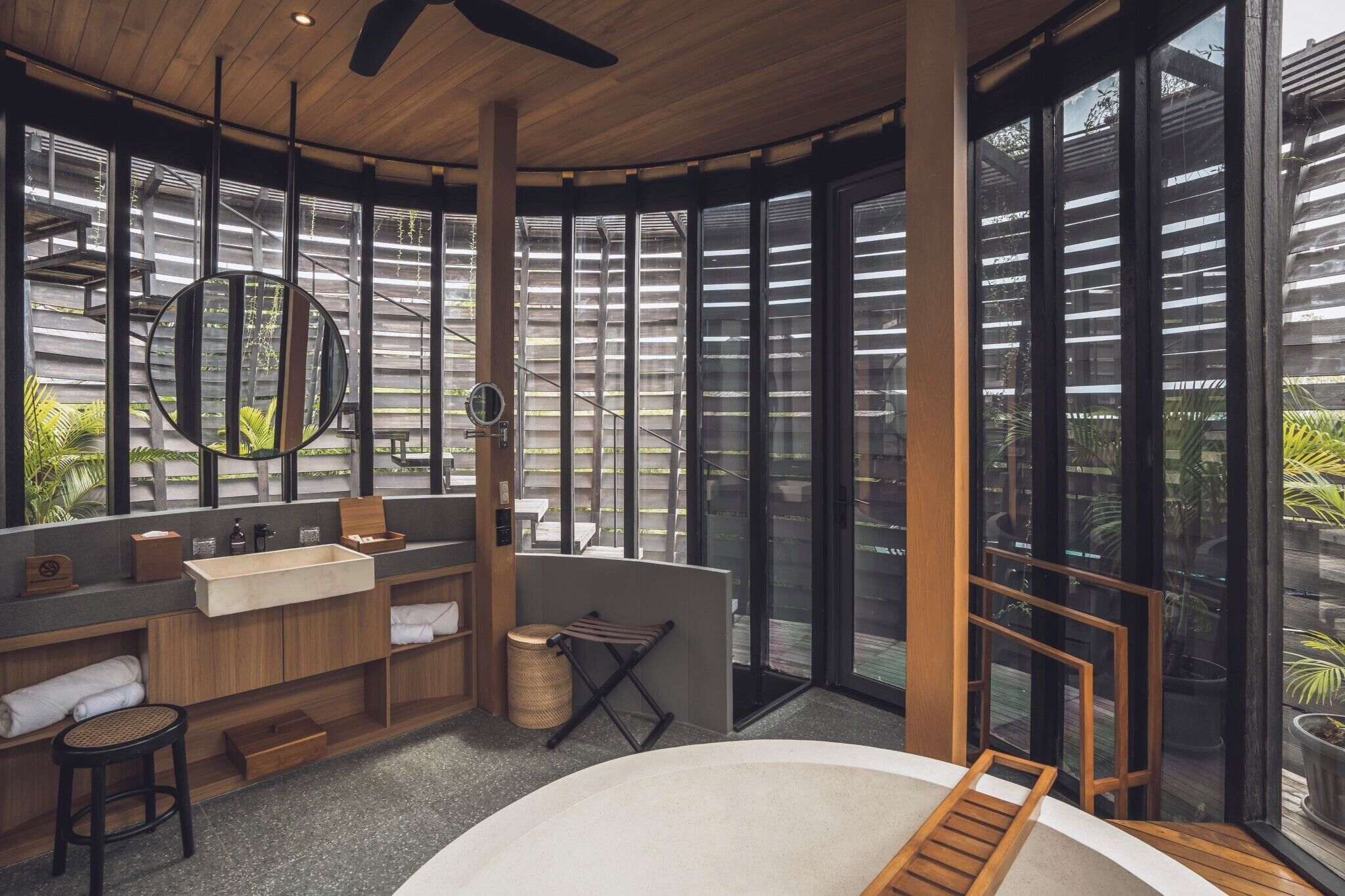 A modern bathroom with a large mirror, wooden vanity, and a view of the outdoors through large windows.