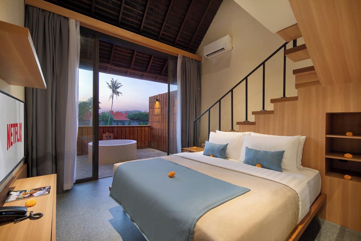 Ein Hotelzimmer mit Bett, Schreibtisch mit Telefon, Fernseher und einem Balkon mit Blick.