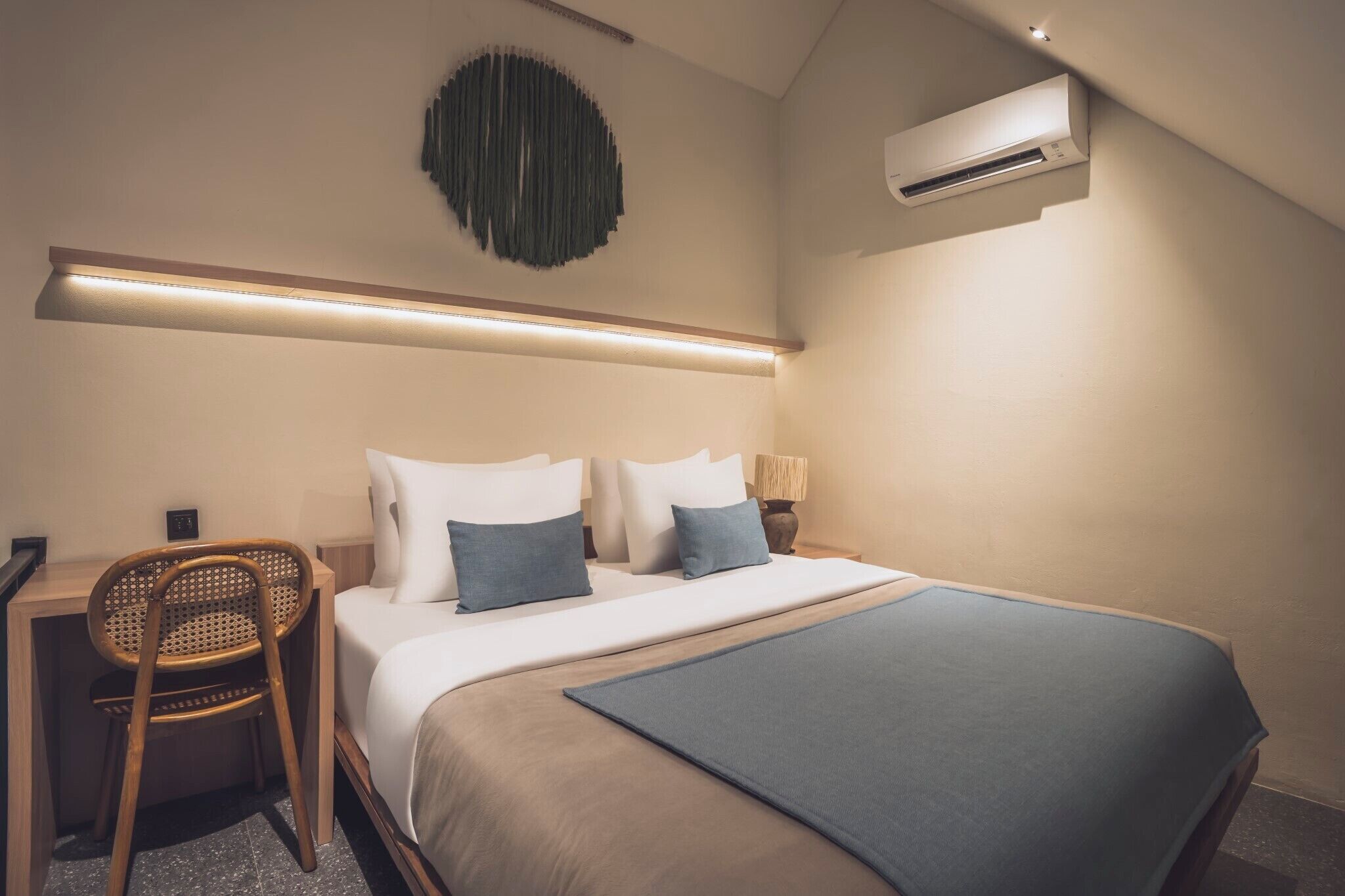 Une chambre d’hôtel moderne avec un lit bien fait, un bureau avec une chaise et un climatiseur fixé au mur.