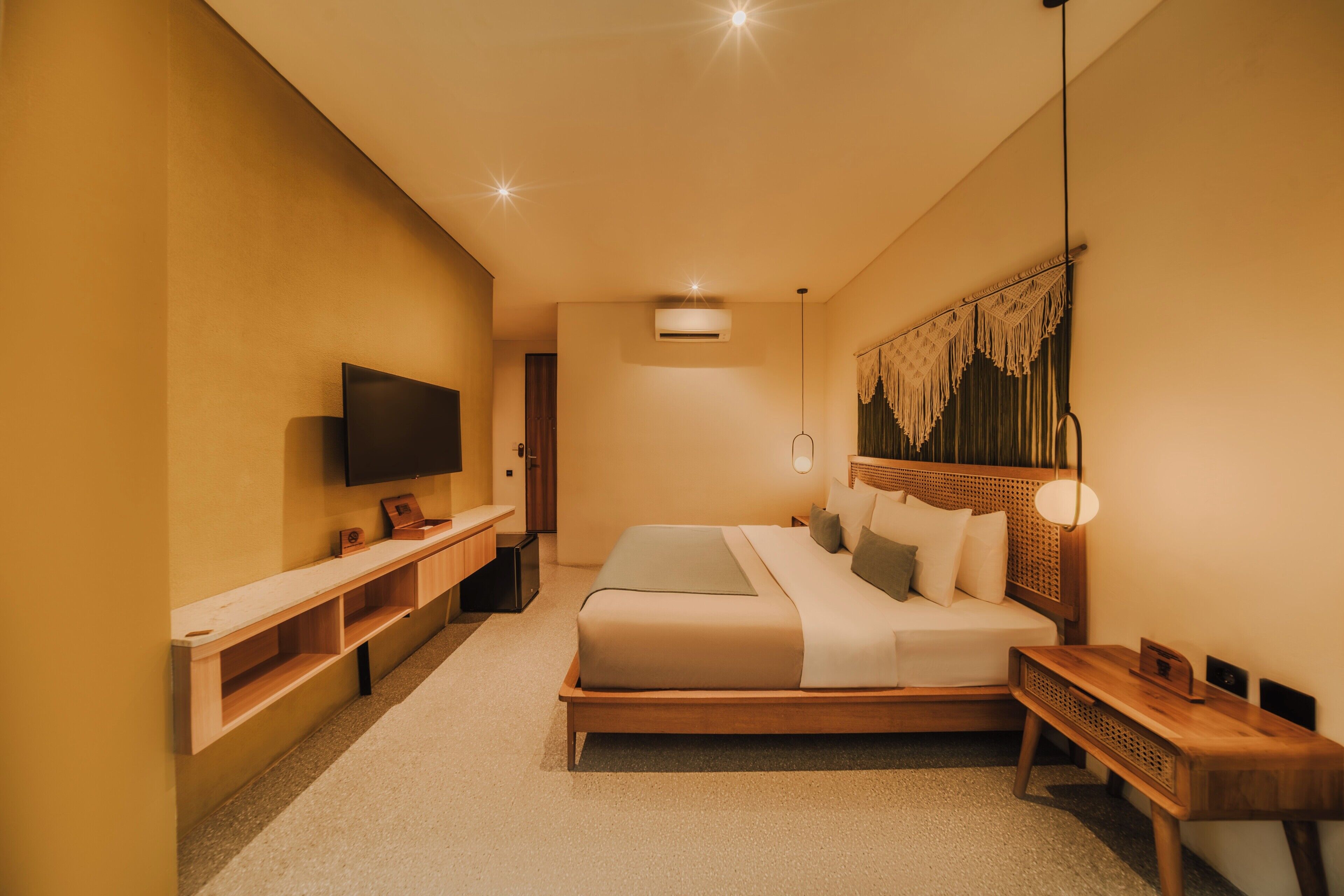 Una habitación de hotel moderna con una cama grande, un televisor de pantalla plana, una mesita de noche de madera y un equipo de aire acondicionado instalado en la pared.