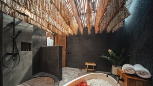 Un baño moderno con ducha de piedra, un banco de madera y una bañera llena de piedras de colores.